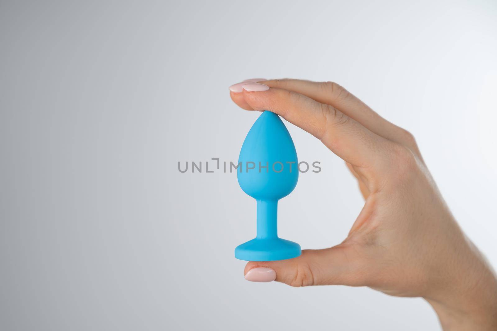 Woman holding a blue anal plug on a white background. Adult toy for alternative sex by mrwed54