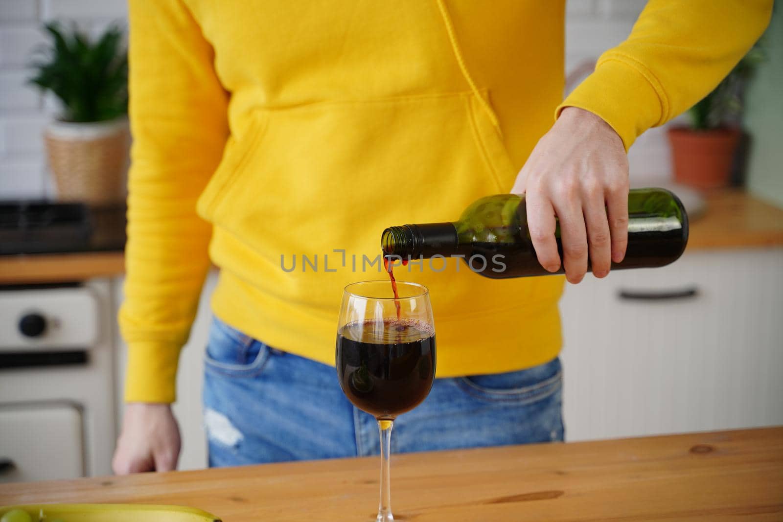 Close up of unrecognizable man pours red wine into glass in kitchen. Unknown guy fills transparent glass with alcohol. by epidemiks
