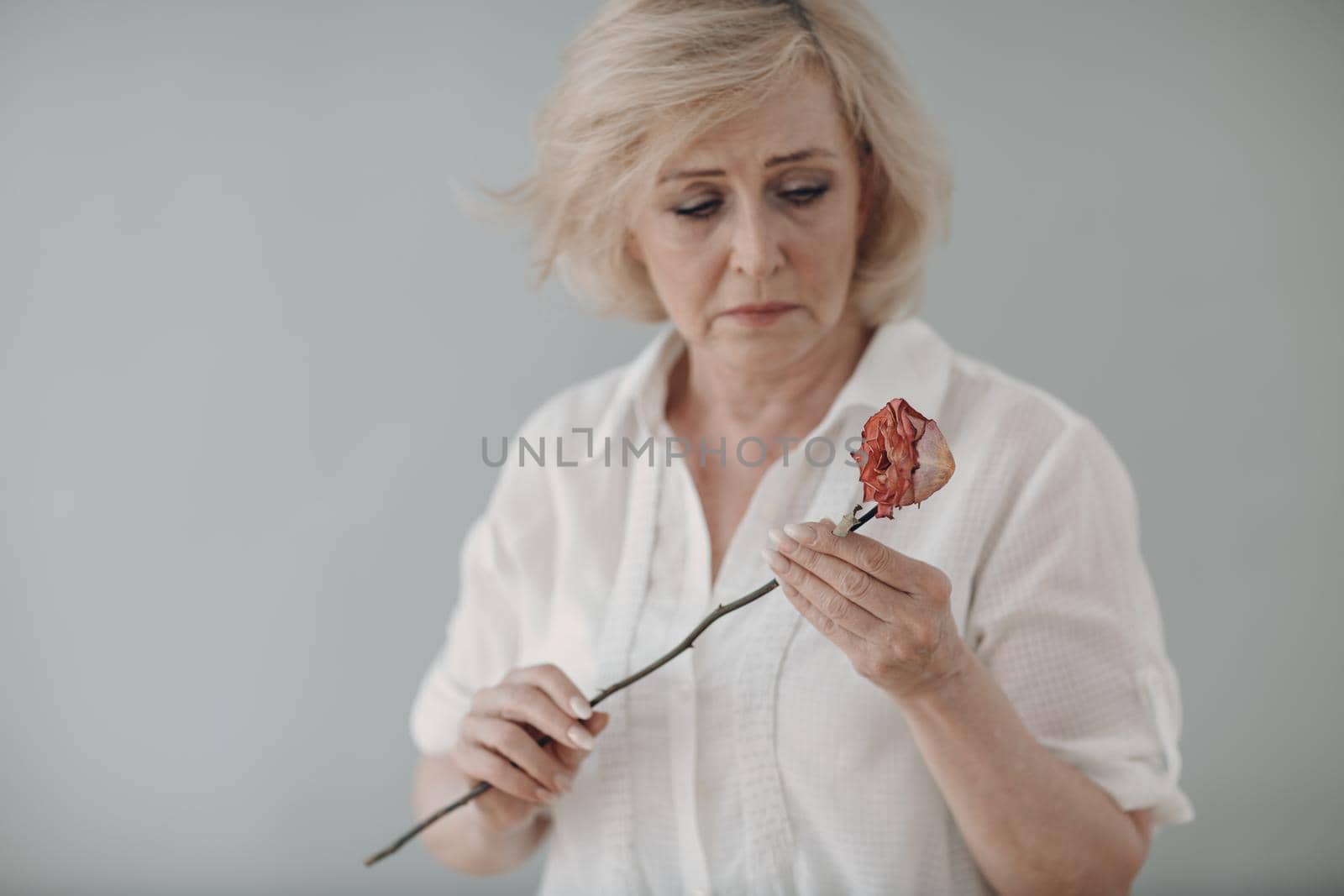 Upset elderly woman in white dressed hold withered one dry old rose flower. by primipil