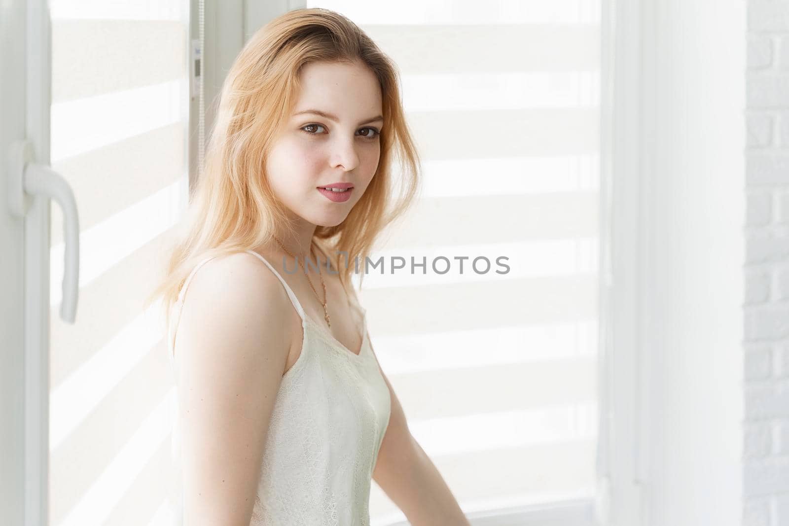 beautiful young woman sitting by the window in a white room