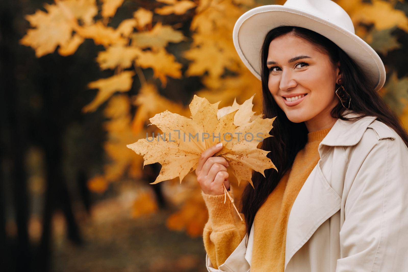 a girl in a white coat and hat smiles in an autumn Park.Portrait of a woman in Golden autumn