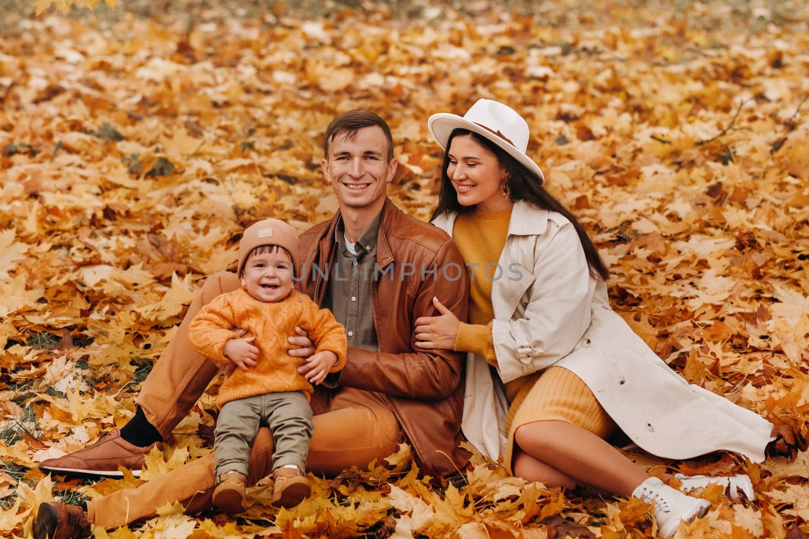 Father and mother with son sitting in the autumn Park. Portrait of a Golden autumn Family in a nature Park