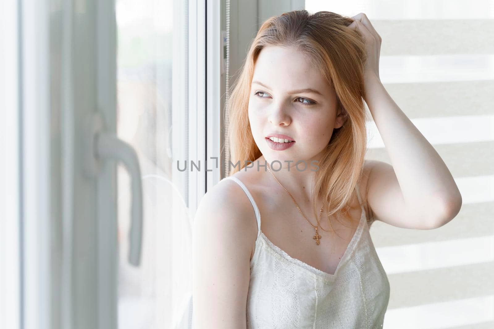 beautiful young woman sitting by the window in a white room by Lena_Ogurtsova