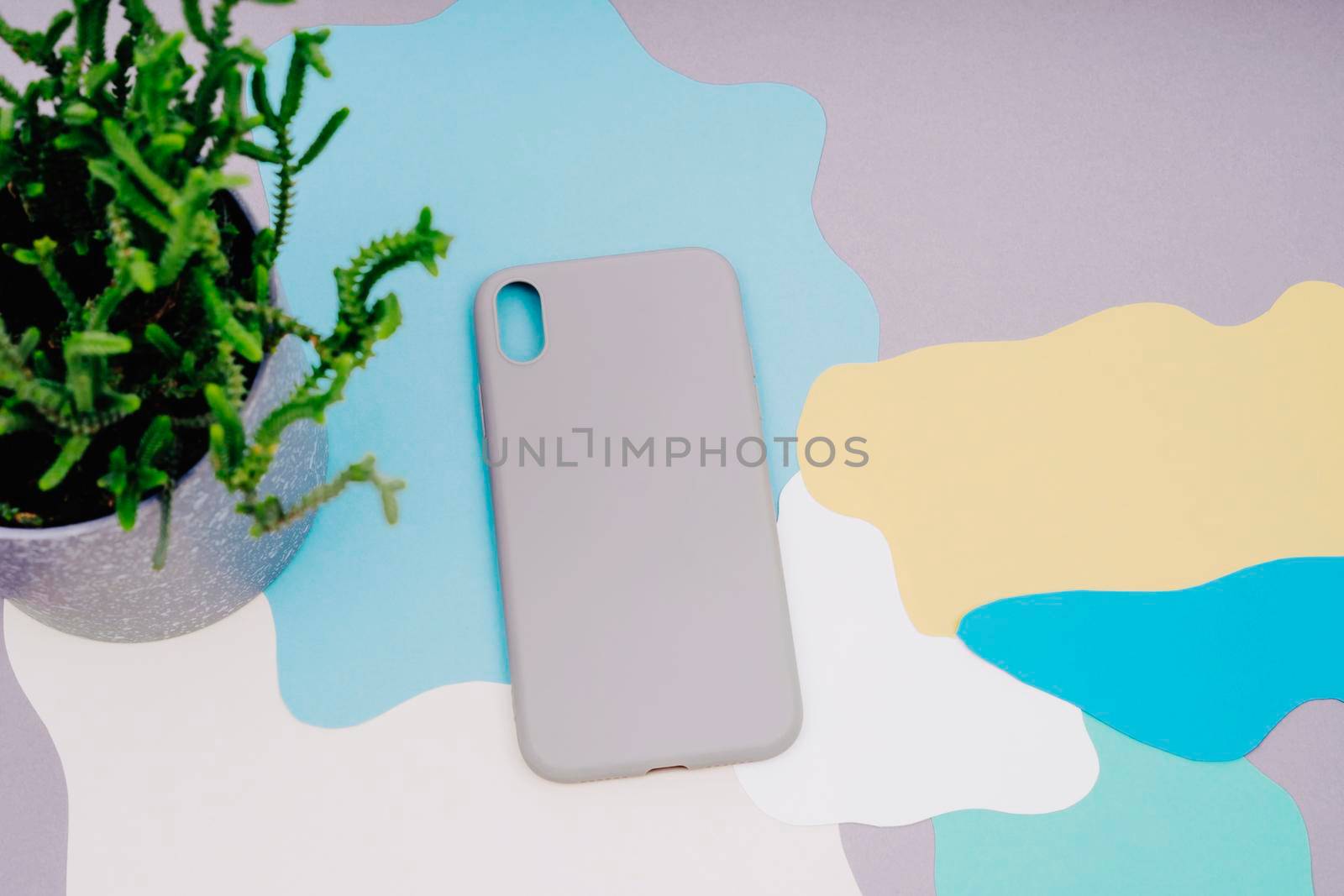 Protective covers for the smartphone. The gray silicone case for the smartphone lies on an abstract background. background of gray, yellow, white, green and blue. Pot with a house plant.