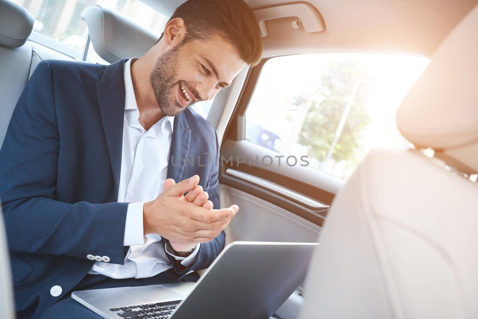 A young man is sitting in the car and enjoying the successful transaction. He looks at the laptop display, which is on his lap