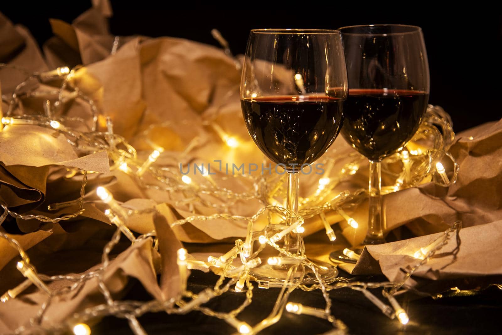 two wine glasses stand in a shining yellow garland on craft paper. cozy romantic celebration