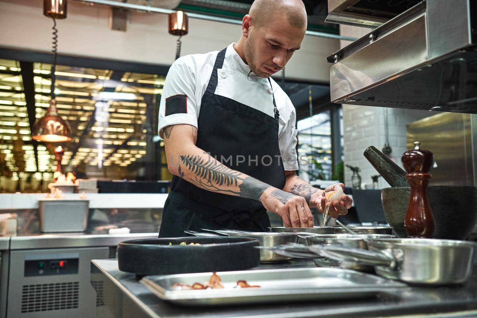 Important ingredient. Concentrated young chef breaking an egg for traditional italian pasta while standing in a restaurant kitchen. Cooking process