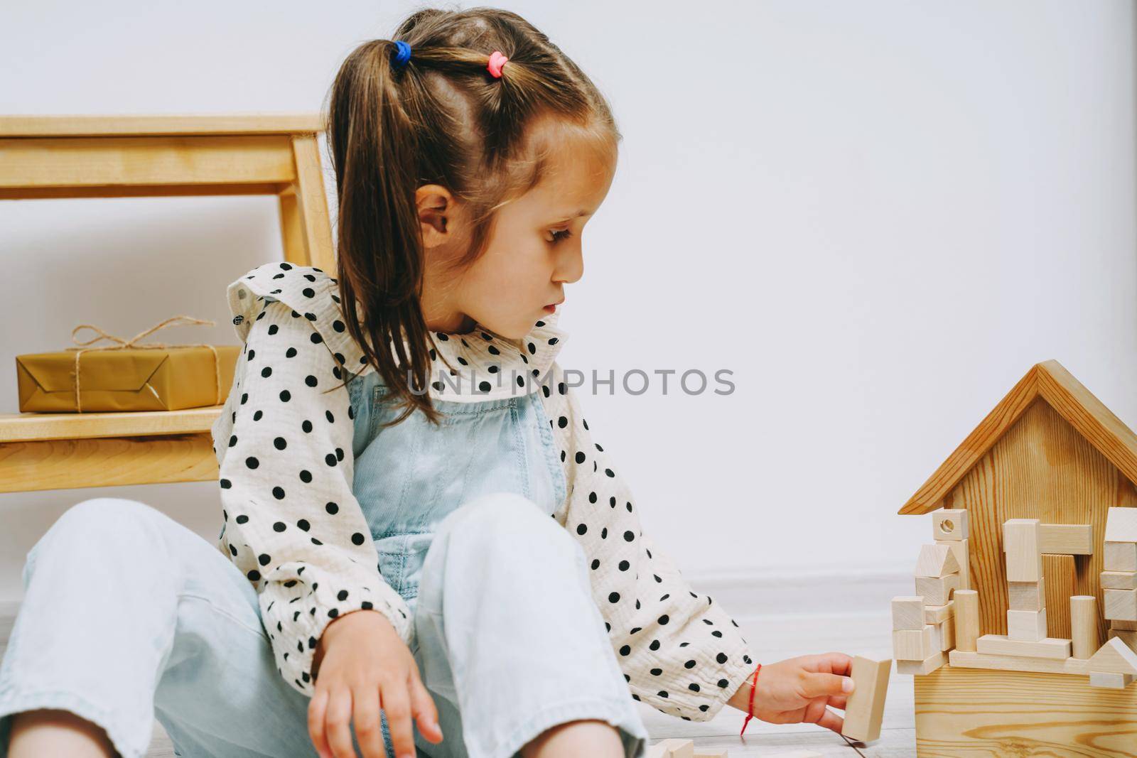 Eco-friendly toys for young children. The girl plays with wooden cubes. Wooden childrens construction kit. The girl carefully builds a tower of small cubes. Eco-toys.