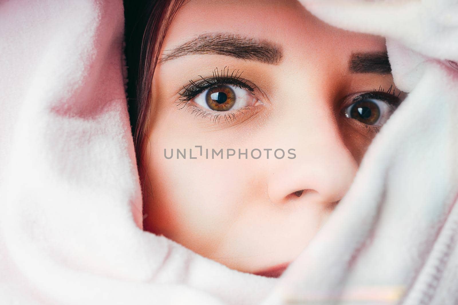 Portrait of young woman looking out of hoodie. Close up of pretty female hiding in sweatshirt and peeking out. by epidemiks