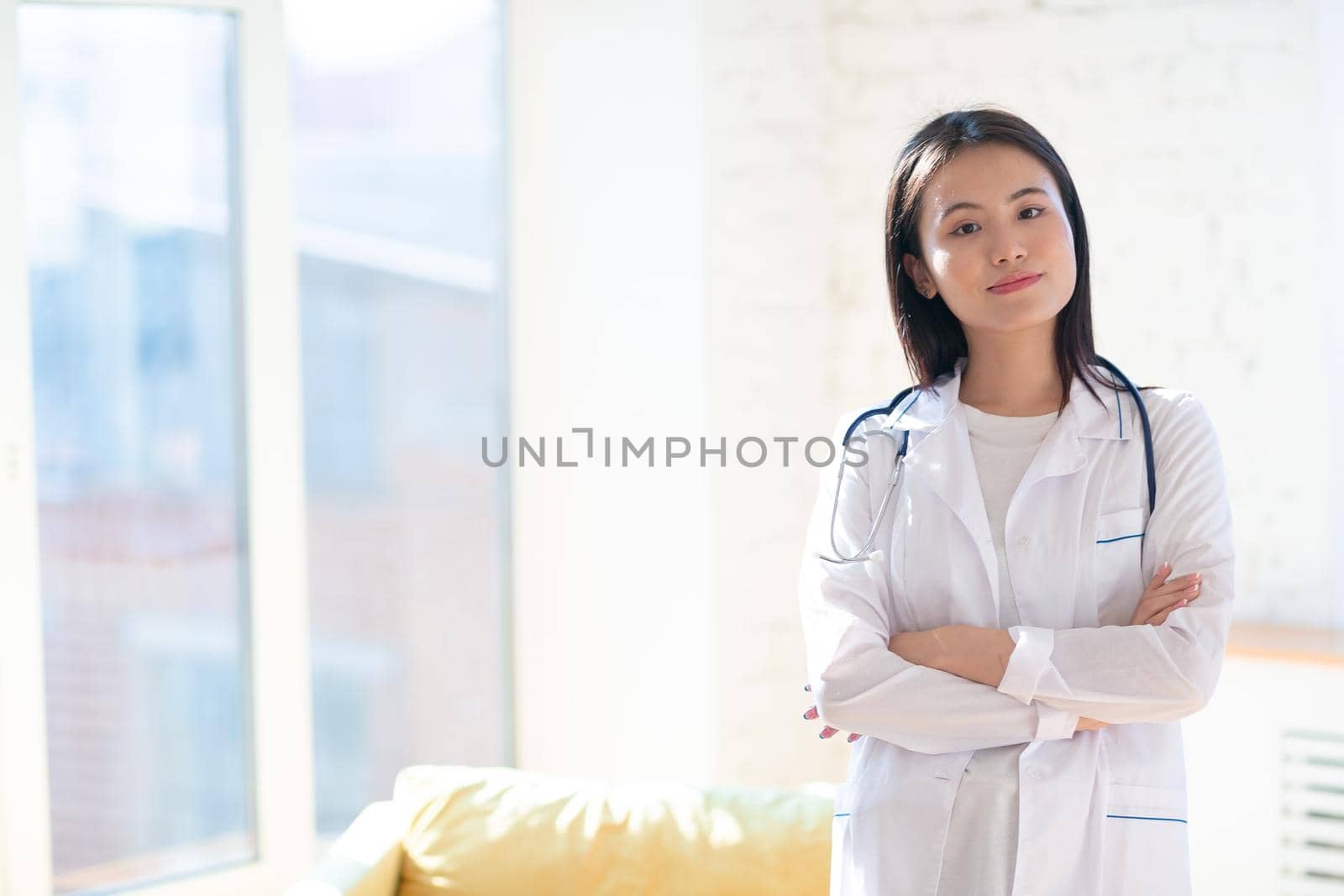 Asian doctor woman in white medical gown with stethoscope against pink background portrait by primipil