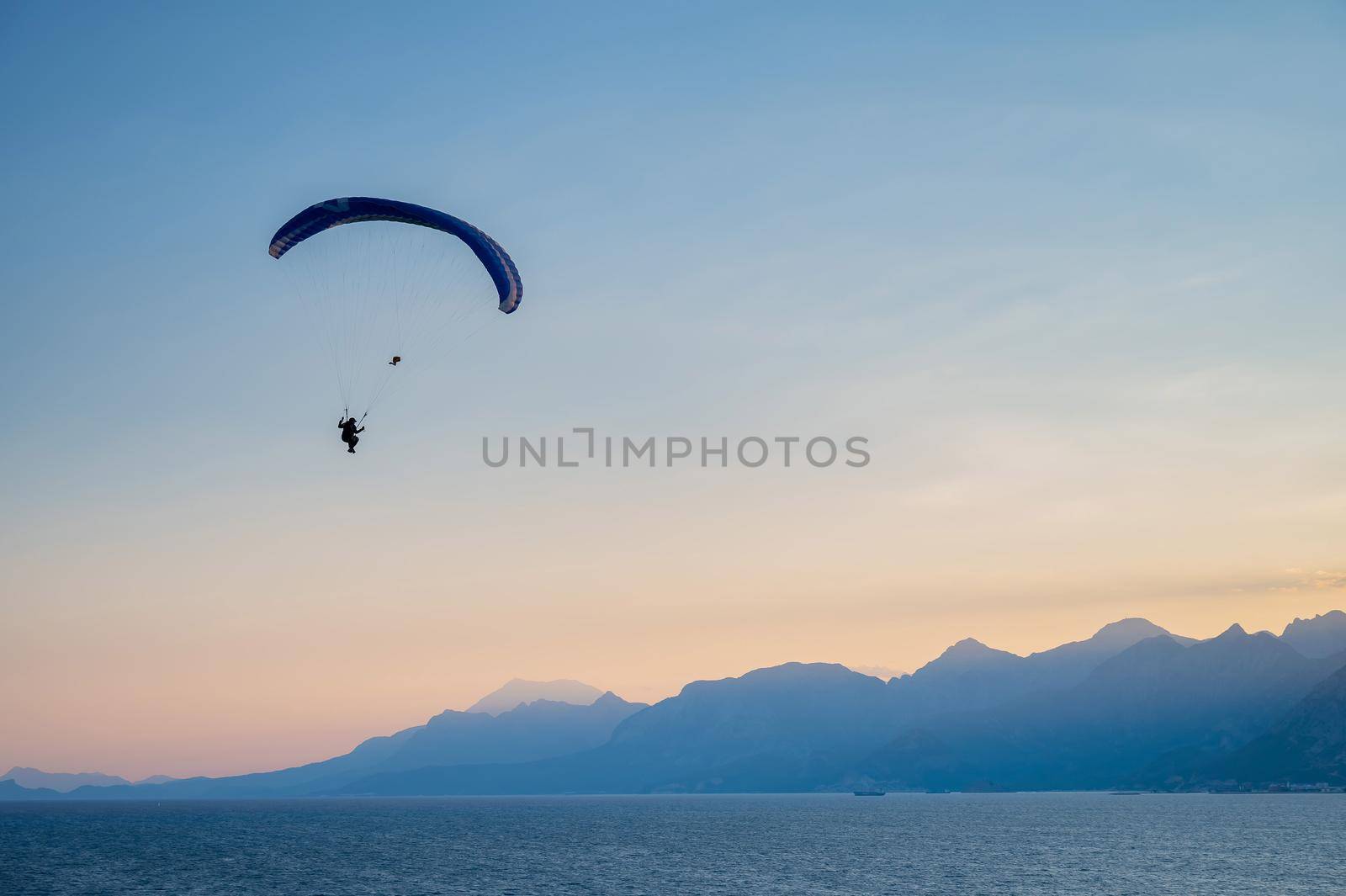 Silhouette of a man on a paraglider flying over the sea at sunset