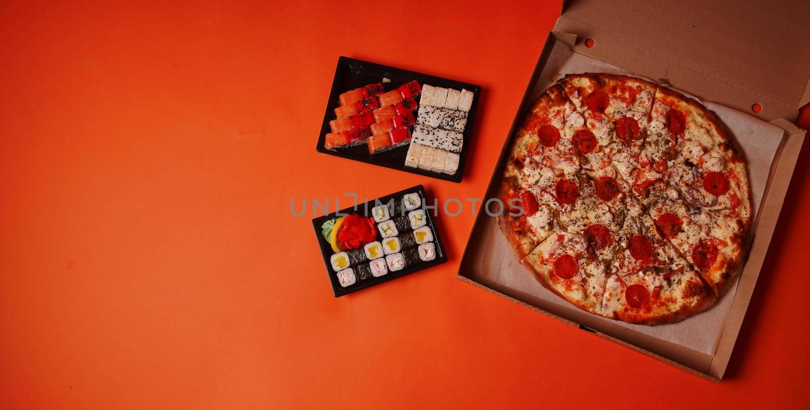 Close up of appetizing sushi in containers and large pizza in box on orange background. Pizza and set of tasty sushi rolls with different ingredients. by epidemiks