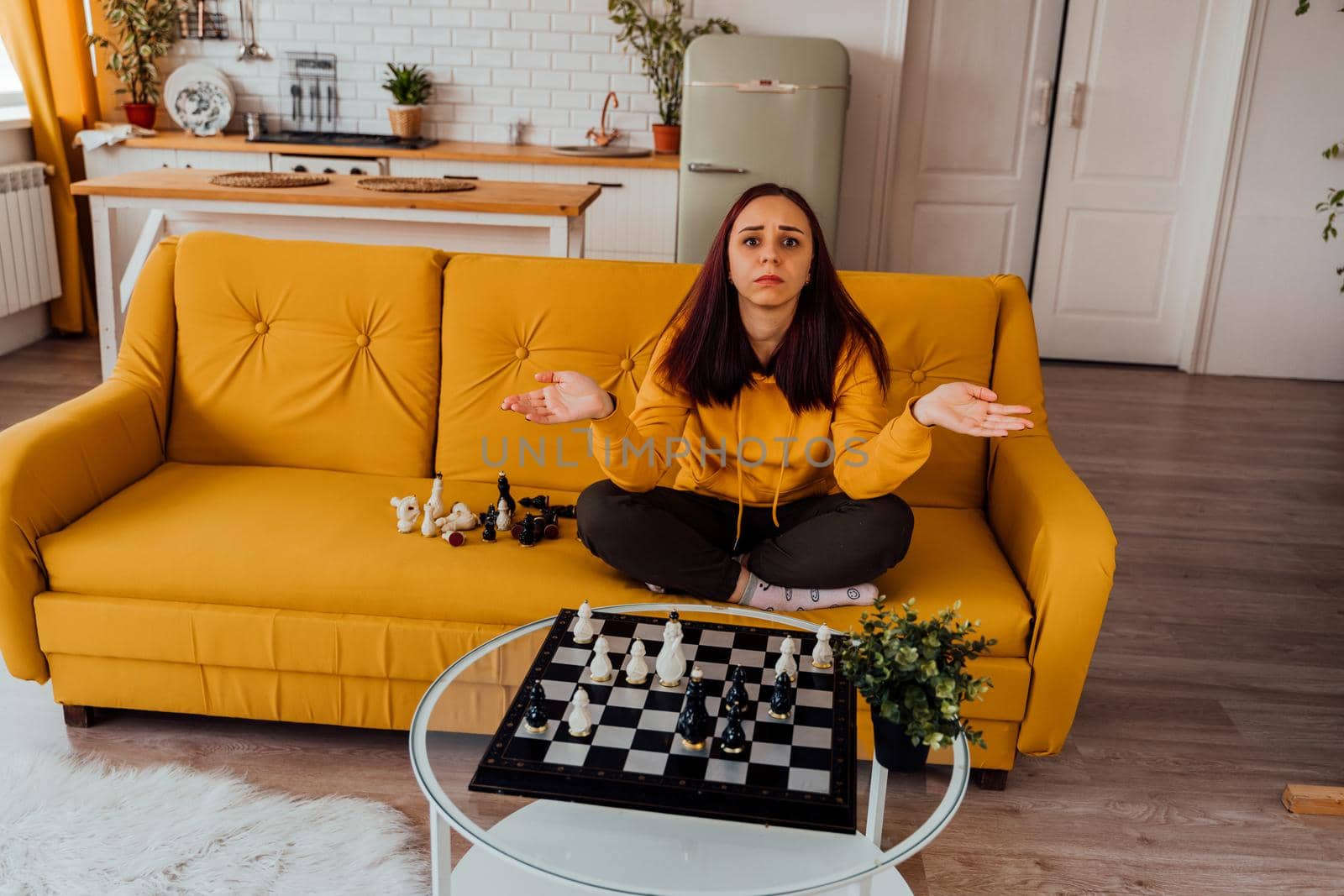 Young upset woman playing chess sitting on sofa. Distressed female plays in logical board game with herself in room. by epidemiks