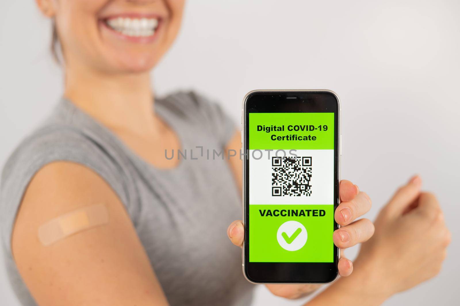 Woman with a plaster on her shoulder after vaccination and demonstrates the QR code on a smartphone