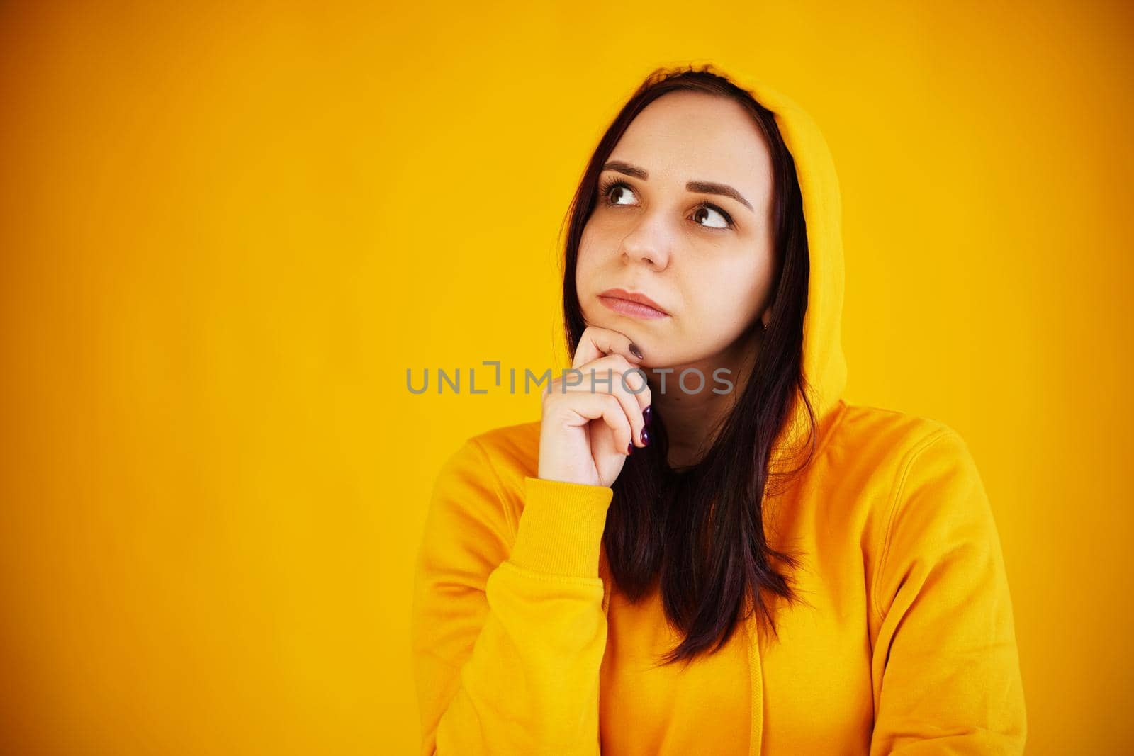 Portrait of young woman on yellow background. Pretty brunette in yellow hoodie posing on bright background