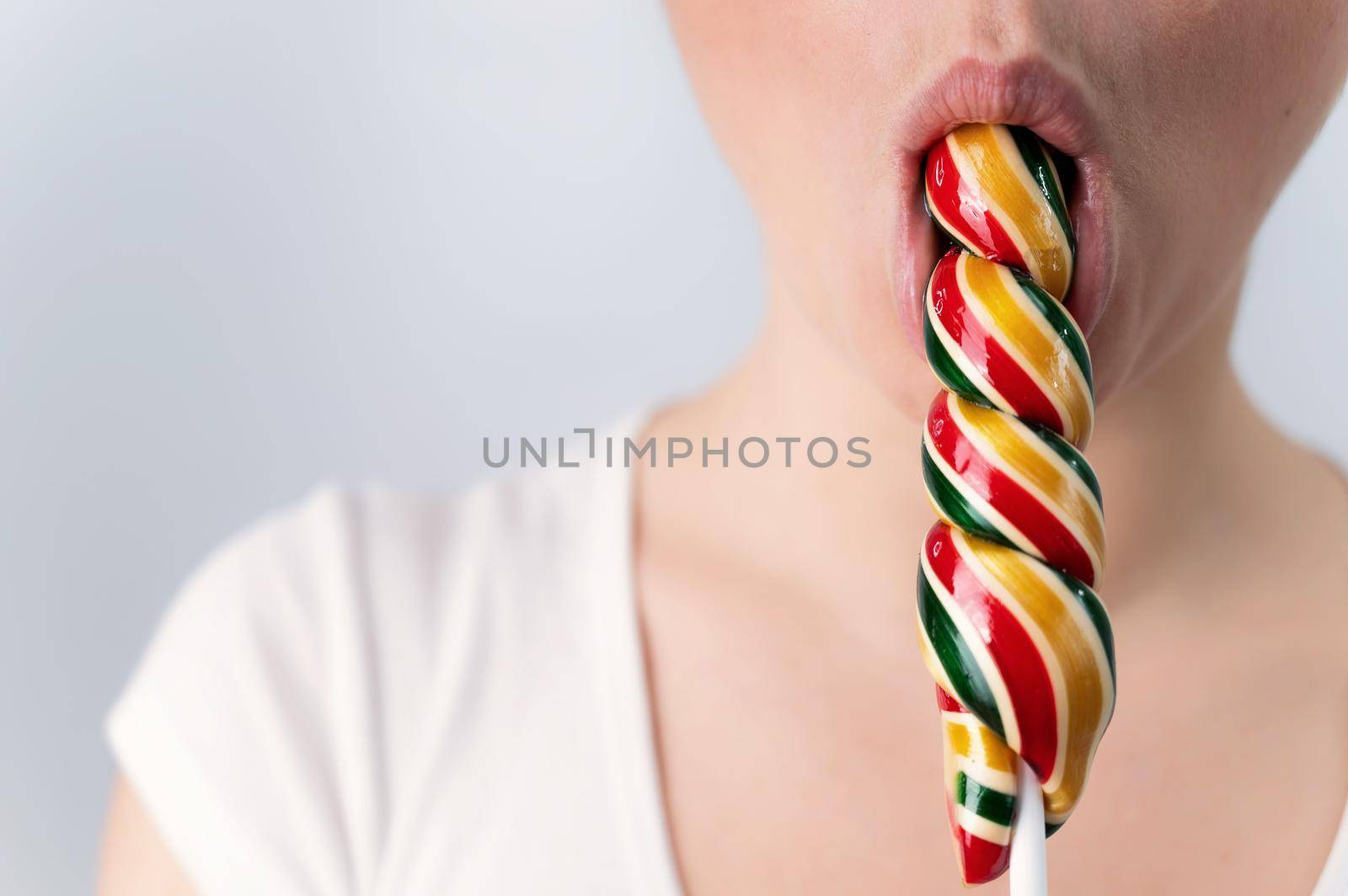 Close-up portrait of a woman sucking a long lollipop against a white background. Blowjob simulation by mrwed54