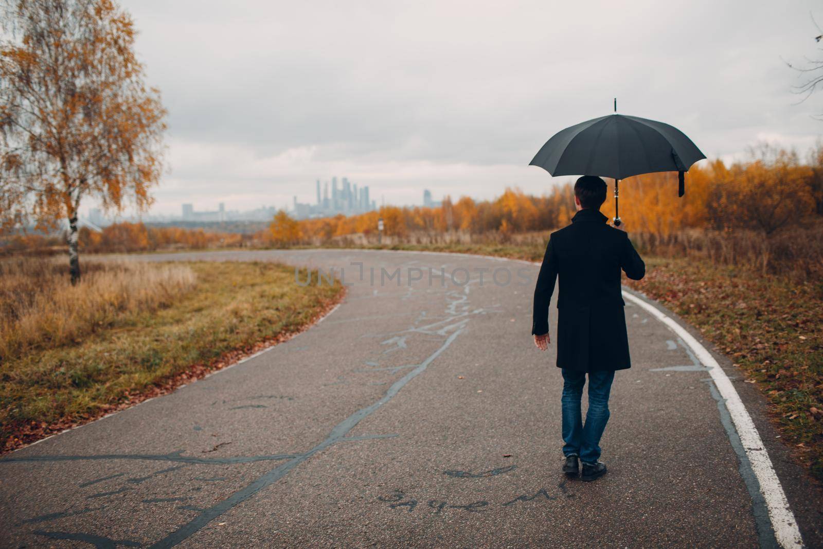 Young man in black coat walking in the rain with umbrella