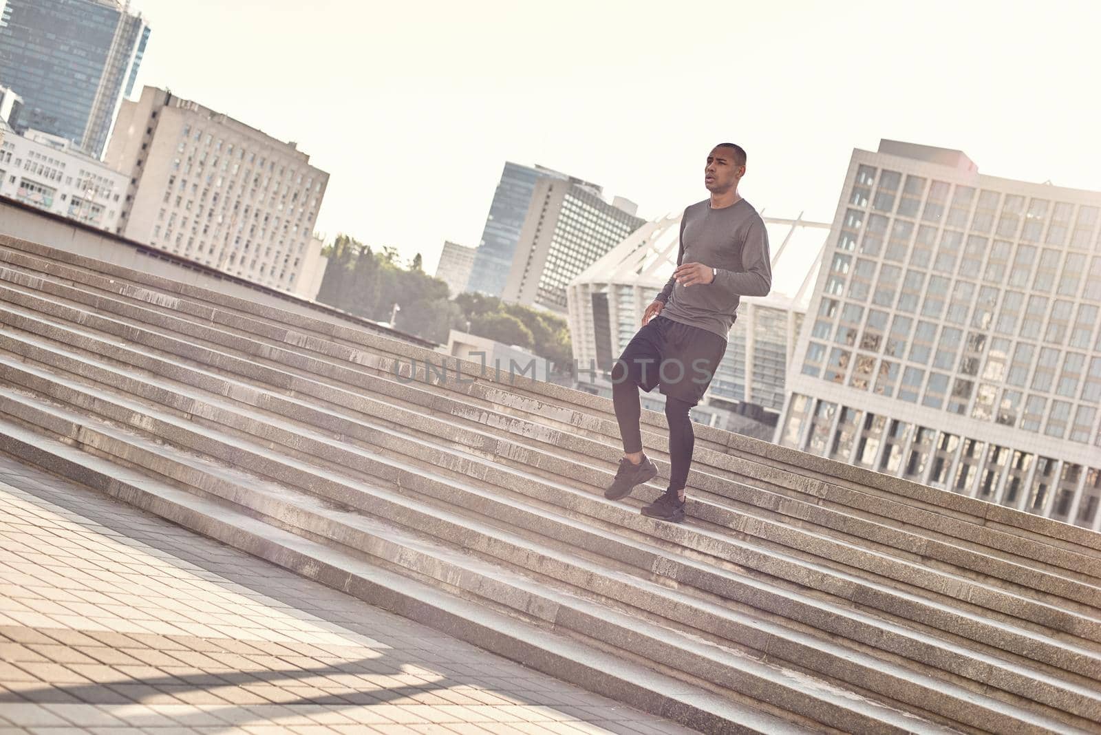 Sport in my life. Full length portrait of athletic african man in sportswear jogging down stairs in the urban environment on a sunny warm day. Cardio training. by friendsstock