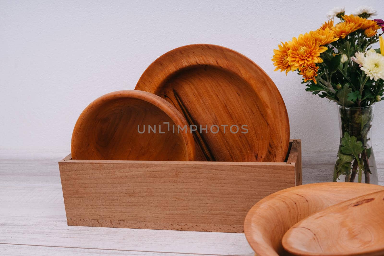 Wooden dishes in a box and a bouquet of autumn flowers. Plates made of natural material. Chrysanthemums.