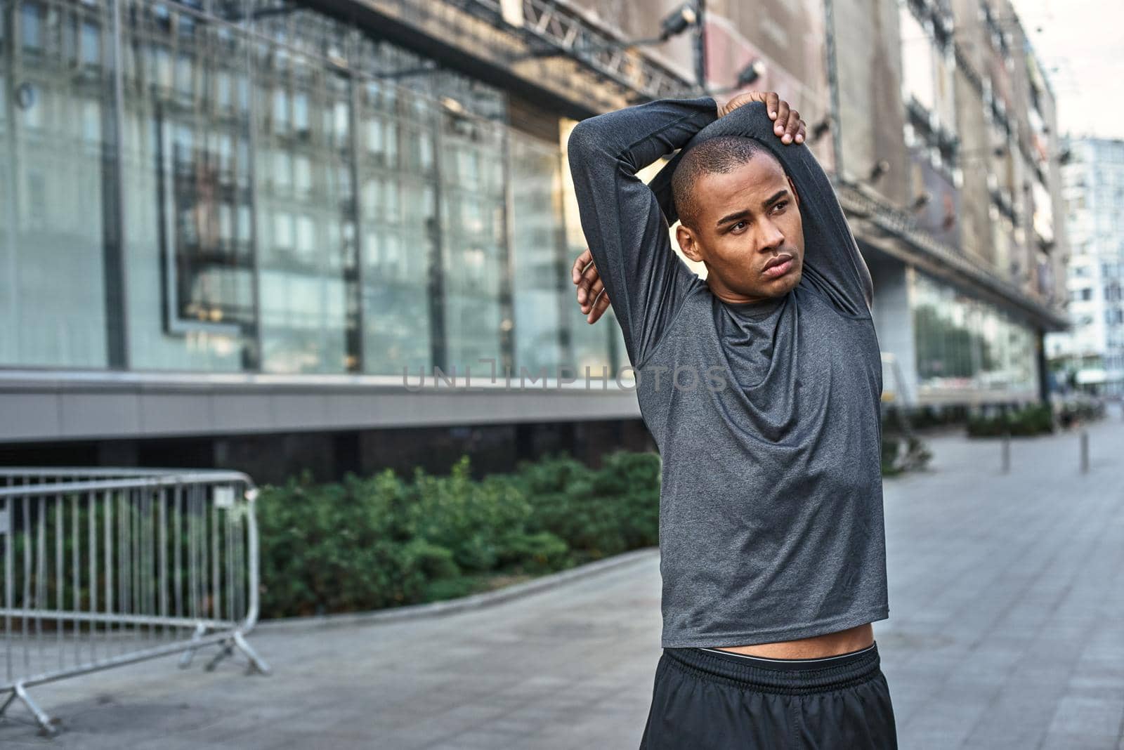 Stretching before great morning workout. Close up portrait of athletic african man standing outside and stretching his arms before training. Cardio training. Healthy habbits. Sport motivation concept. Fitness concept.