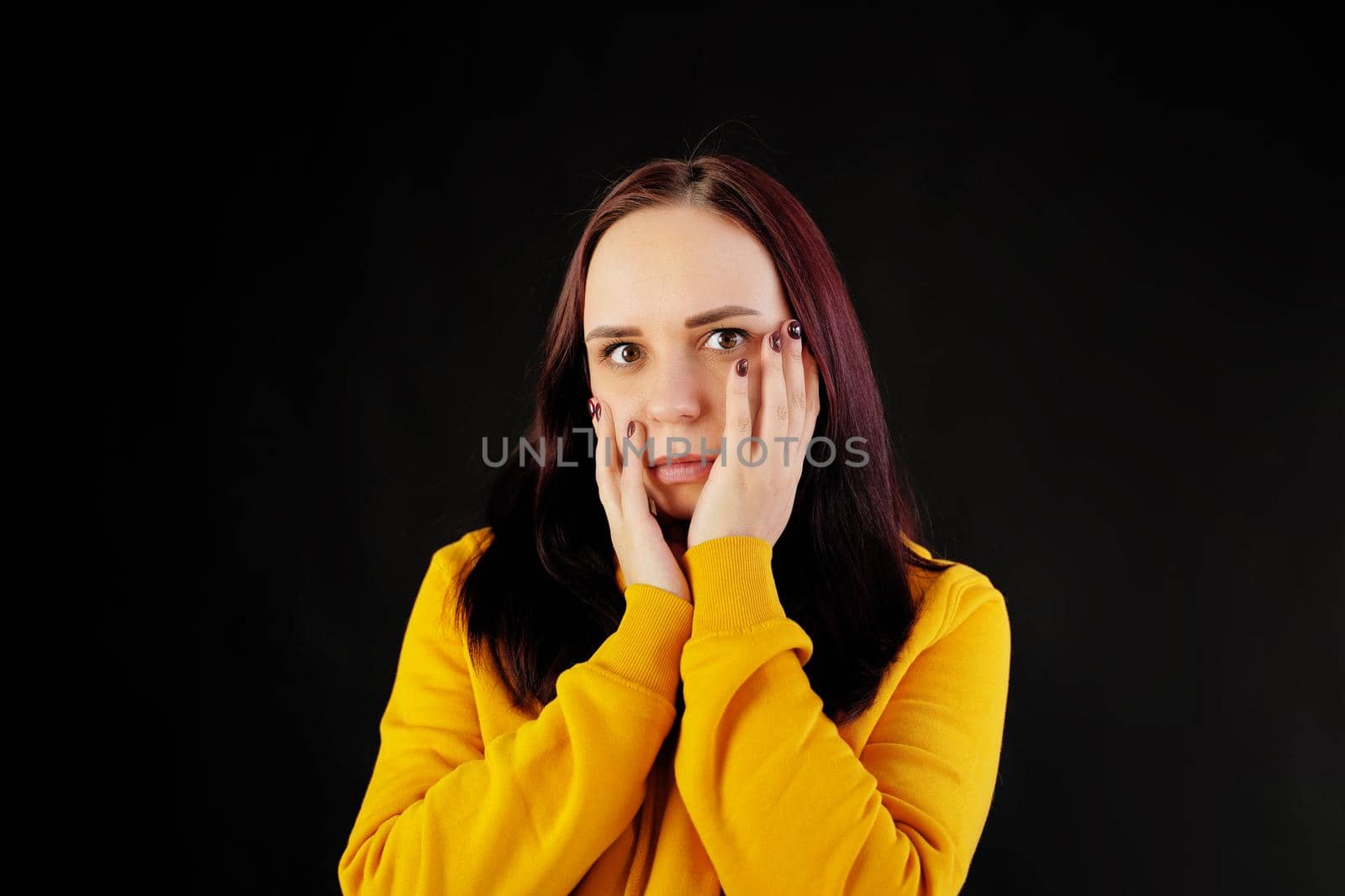Portrait of young woman on black background. Pretty brunette in yellow hoodie posing on dark background. by epidemiks