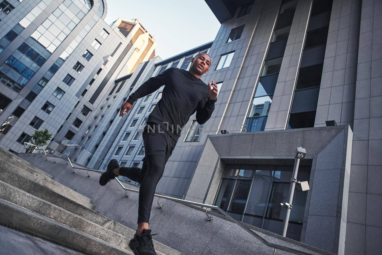 Cardio training. Full length of young african man in sportswear running in the morning against modern buildings of the city. Workout. Sport concept. Health concept