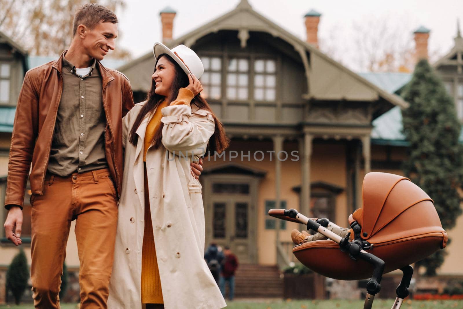 Father and mother on a walk with a stroller in the autumn Park on the background of the estate. A family walks through the Golden autumn nature Park. by Lobachad