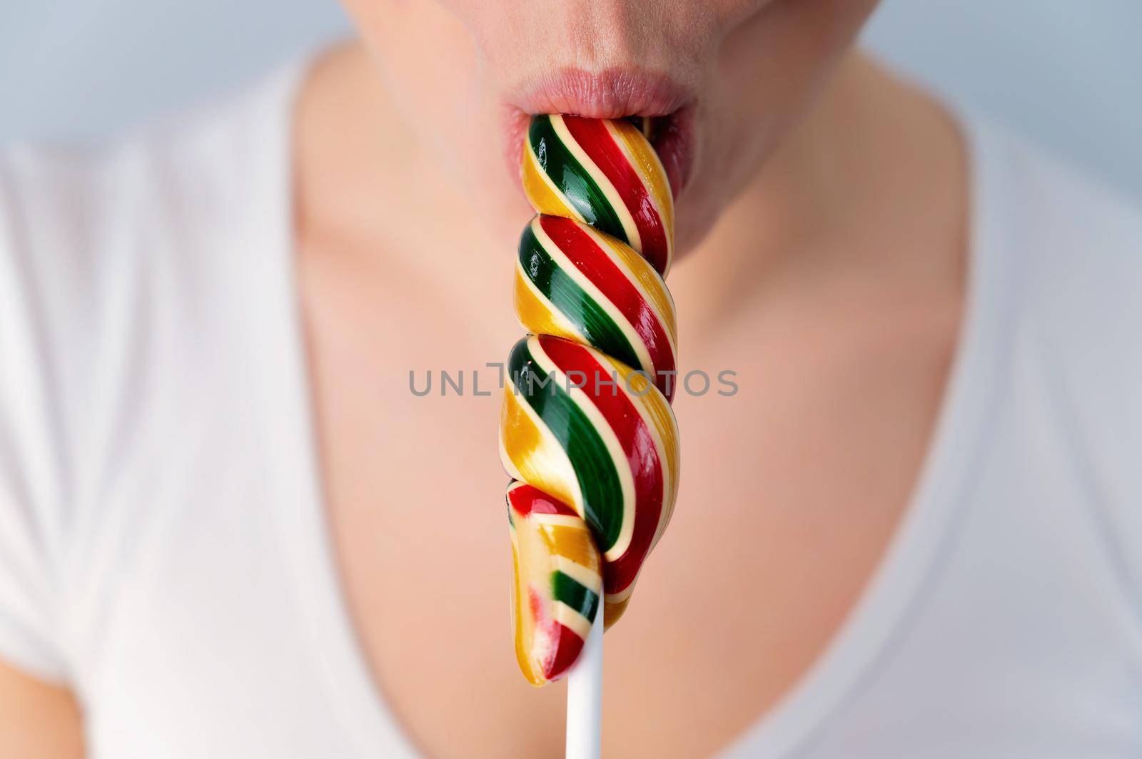 Close-up portrait of a woman sucking a long lollipop against a white background. Blowjob simulation.