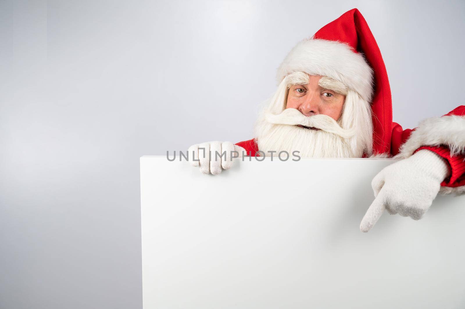Santa Claus points to an empty white space. Promotional offer for Christmas