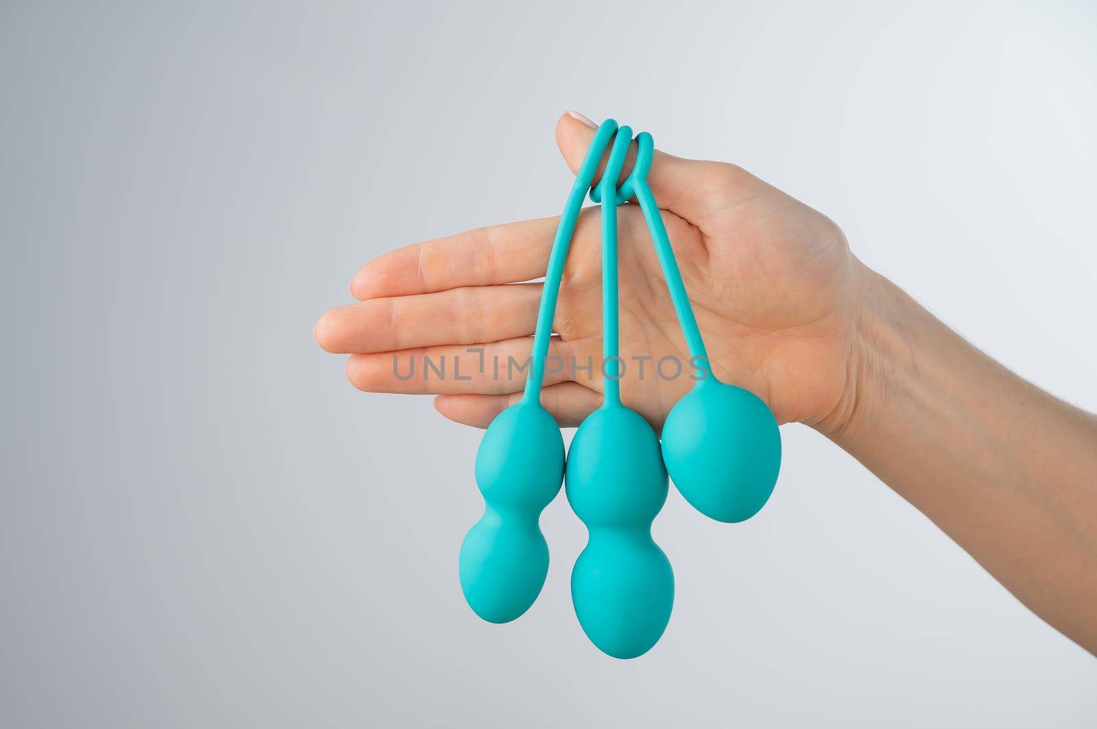 A faceless woman demonstrates a set of mint-colored vaginal balls. Girl holding a kegel trainer for training pelvic floor muscles on a white background. by mrwed54