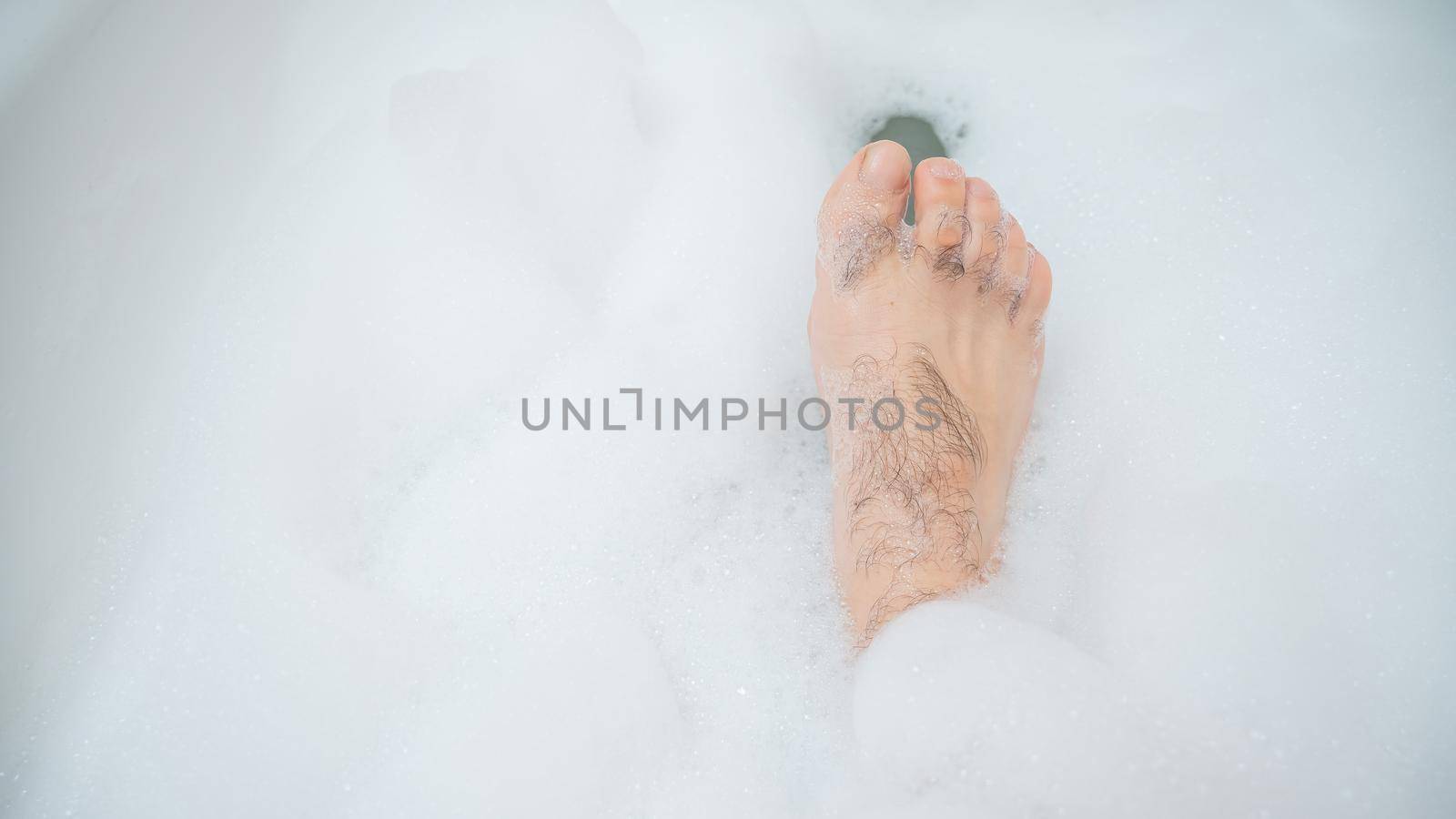 Funny picture of a man taking a relaxing bath. Close-up of male feet in a bubble bath.