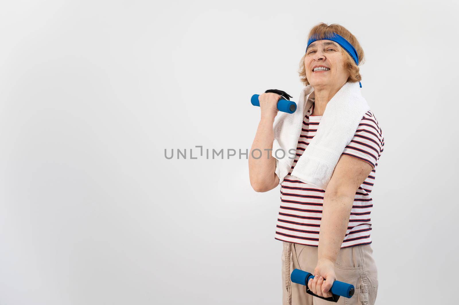 An elderly woman with a blue bandage on her head trains with dumbbells on a white background.