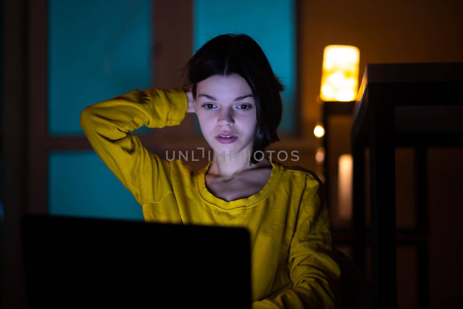 Portrait of beautiful caucasian girl uses laptop while sitting at home. In the evening creative woman works on a computer in her cozy living room.