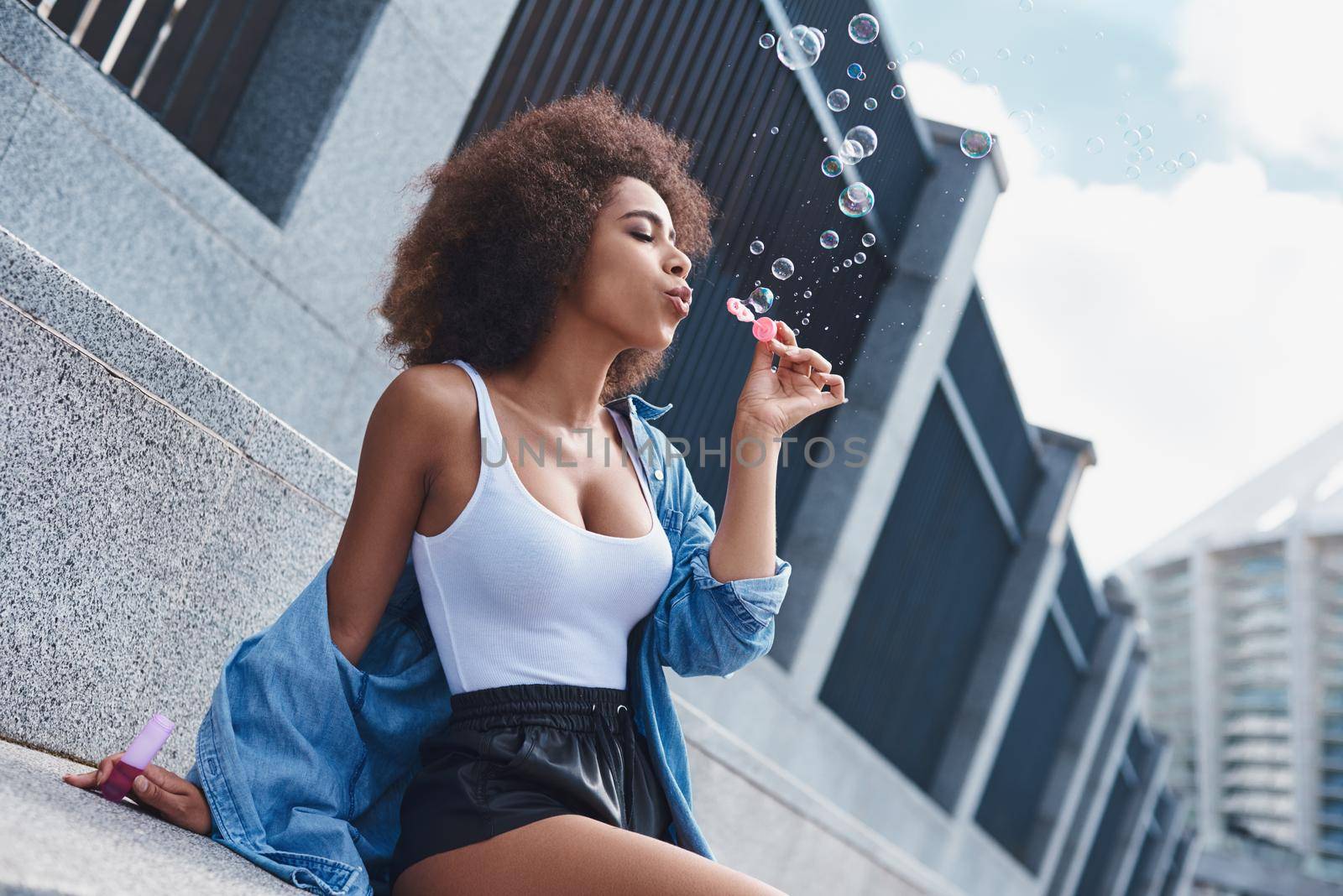 Young woman free style on the street sitting on concrete stairs leaning back blowing bubbles concentrated