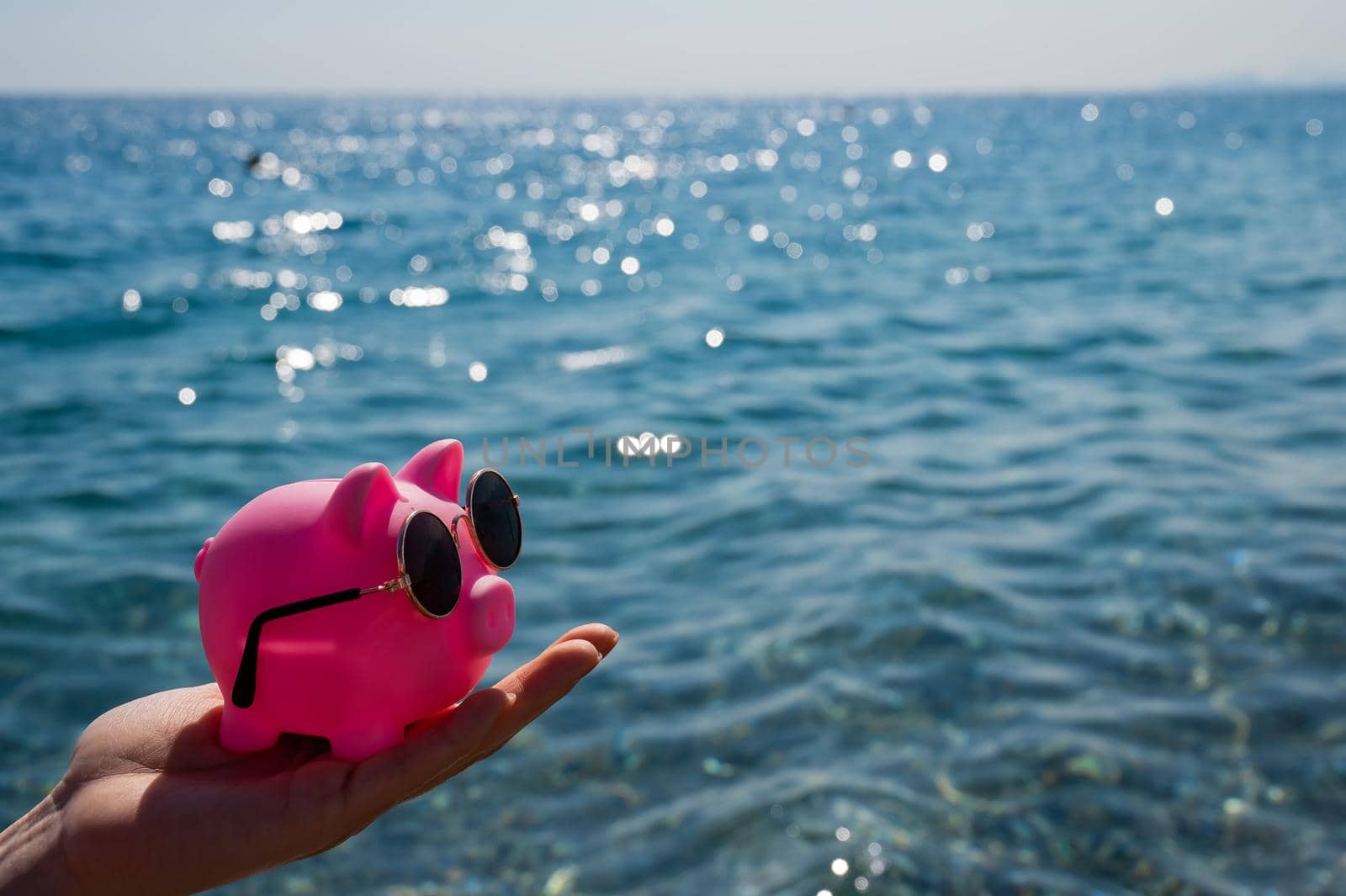 A woman holds a piggy bank in sunglasses on the background of the sea. Budget vacation