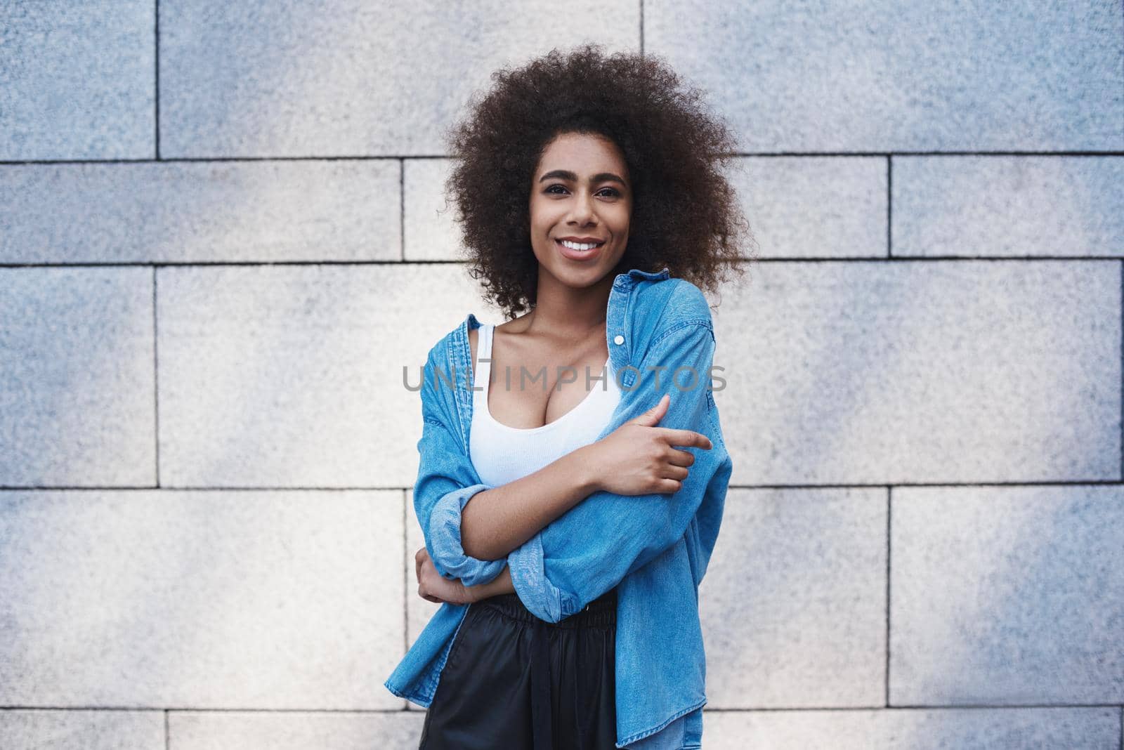 Young woman free style on the street standing isolated on concrete wall hugging herself looking camera smiling cheerful