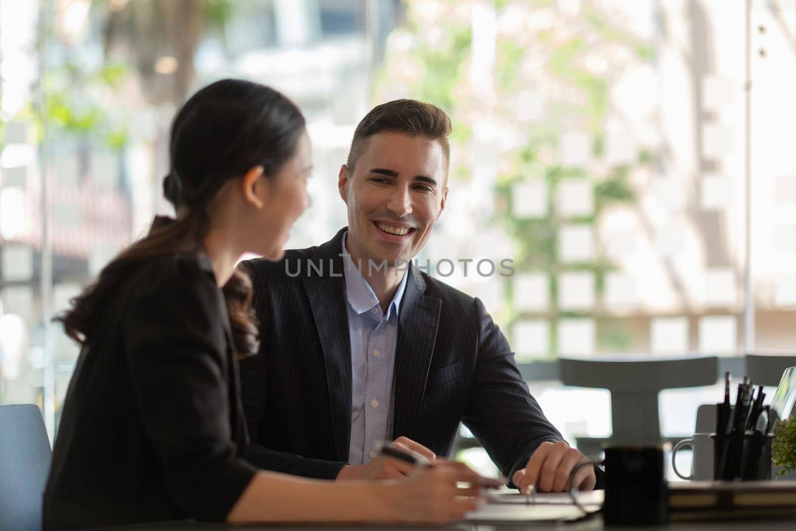 Multiethnic male caucasian mentor and female asian sitting at desk with laptop doing paperwork together discussing project financial report. Corporate business collaboration concept by nateemee