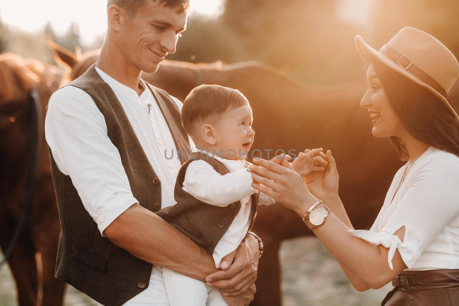 A family in white clothes with their son walking with two beautiful horses in nature. A stylish couple with a child are photographed with horses at sunset.