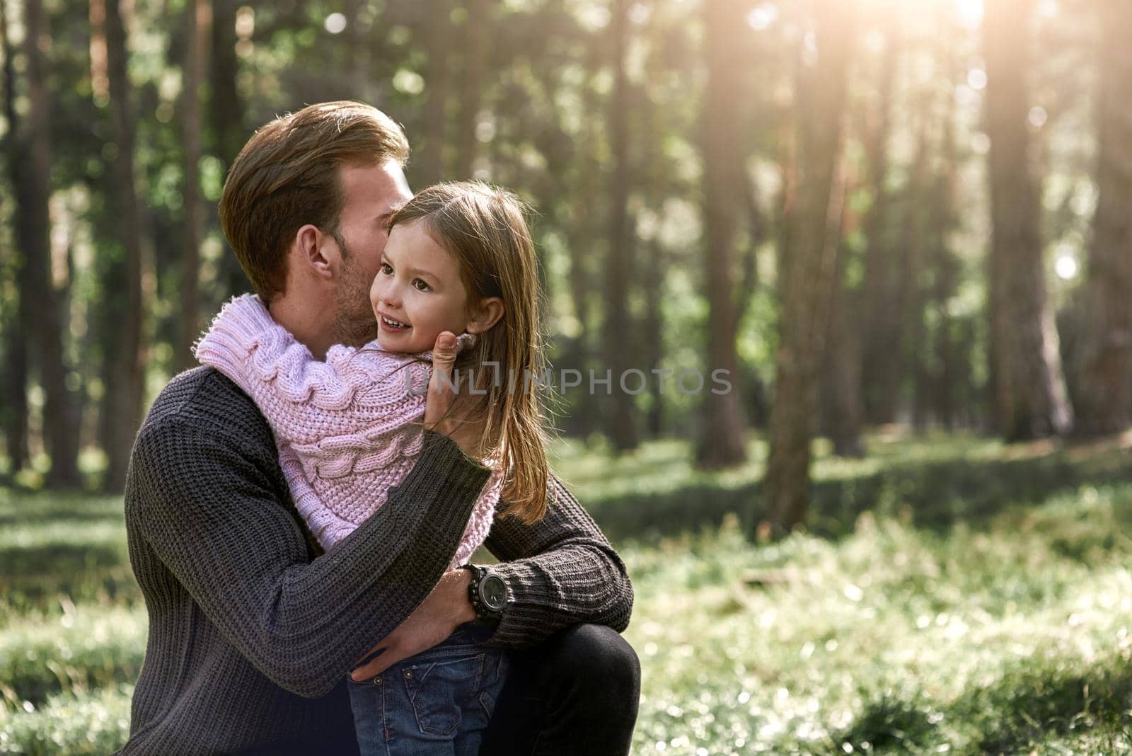 Little girl and her father in the forest. Girl is hugging father. Young man is wearing a dark sweater, girl is in pink bright sweater