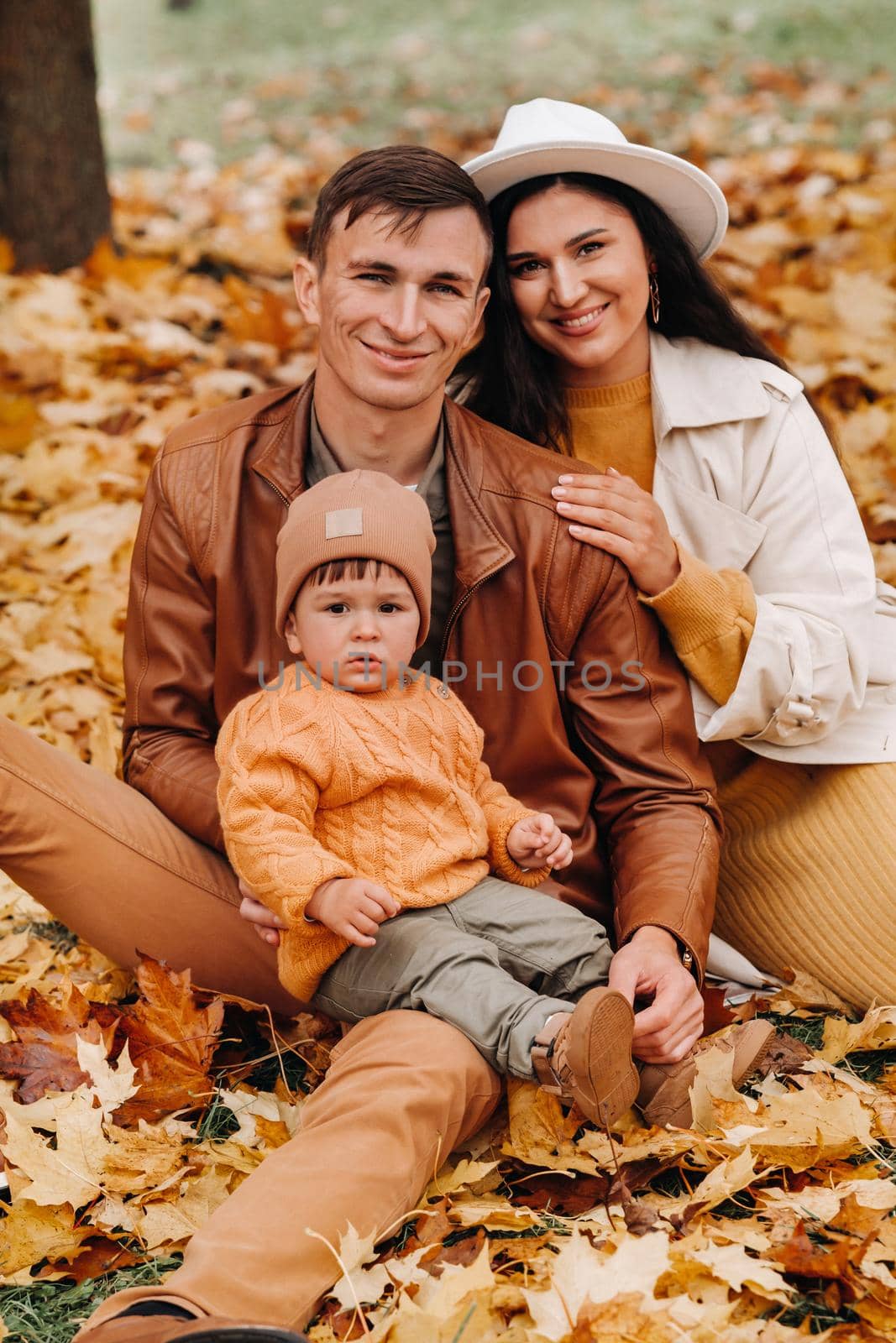 Father and mother with son sitting in the autumn Park. Portrait of a Golden autumn Family in a nature Park. by Lobachad