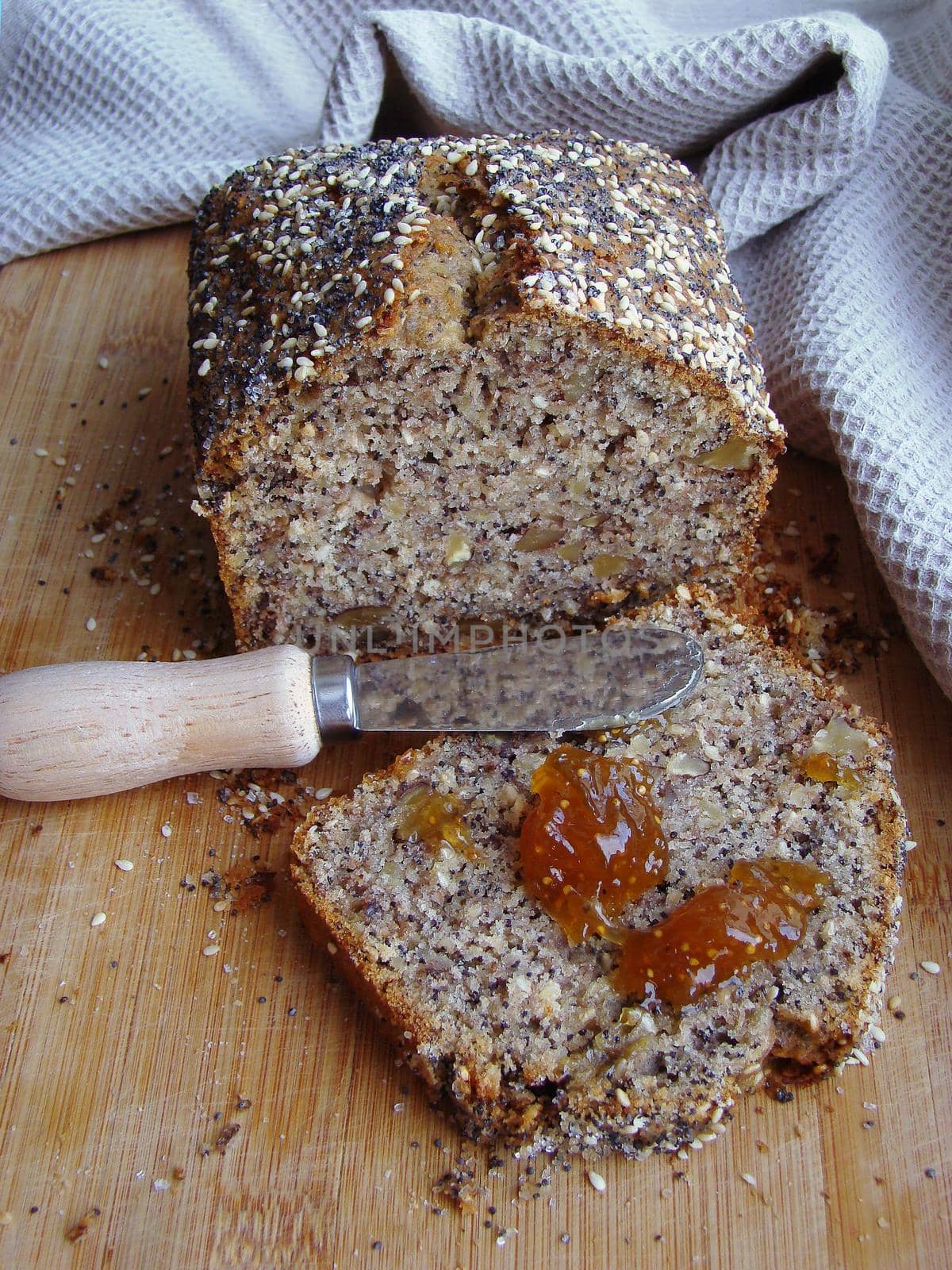 Whole grain organic bread with homemade poppy seeds. Appetizing slice of bread with a portion of jam, small serving knife with wooden handle, wooden surface by Proxima13