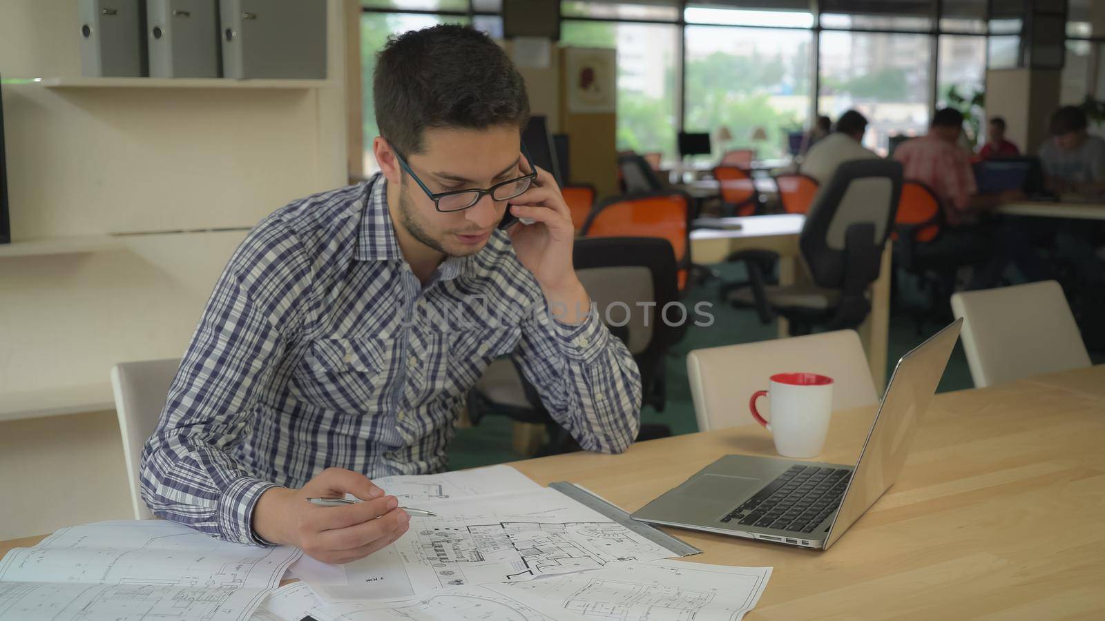 engineer sitting in at the working place on the desk blueprint. young professional man call client talking use smartphone