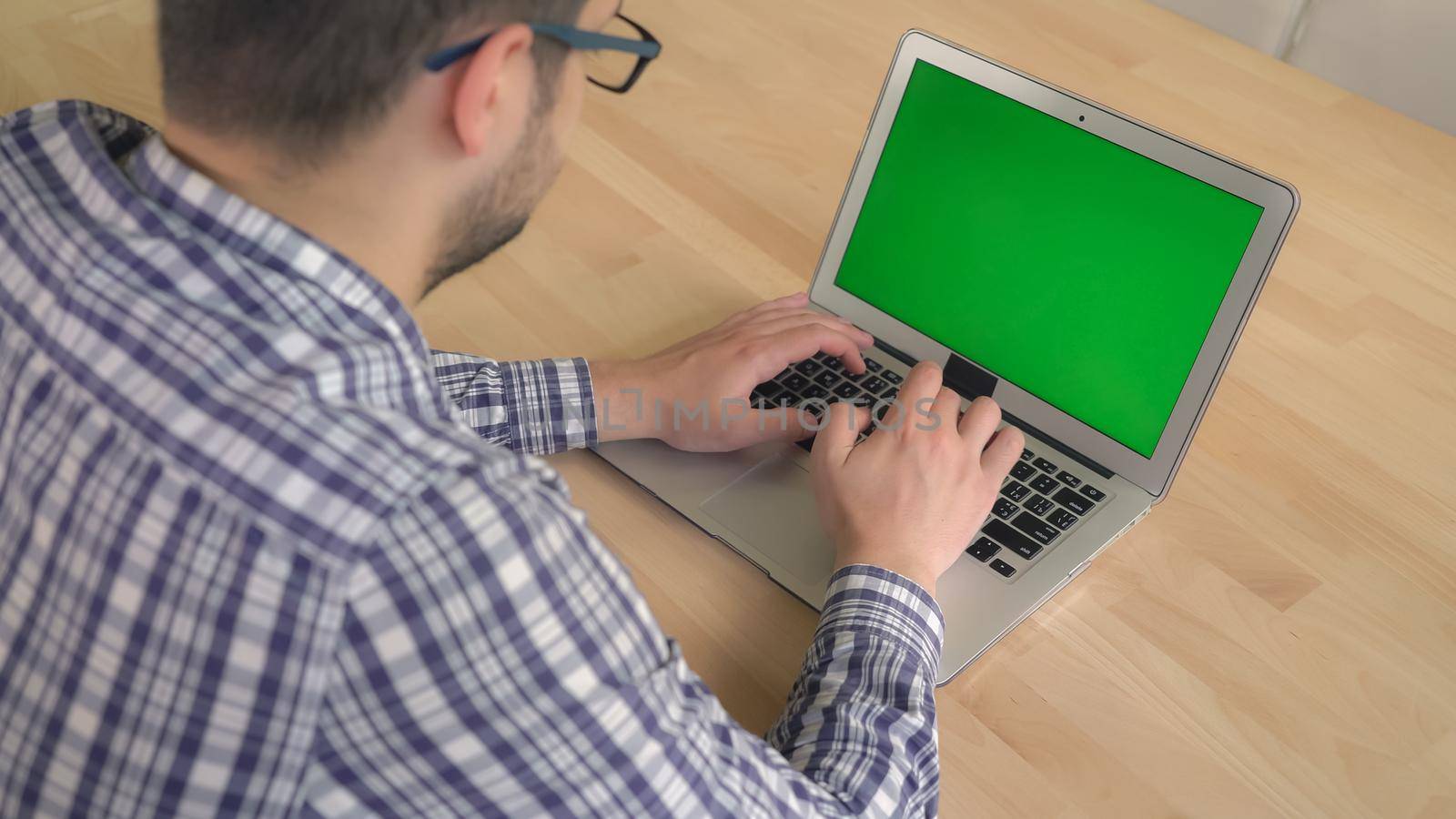 Casual stylish guy typing on keyboard laptop with green screen