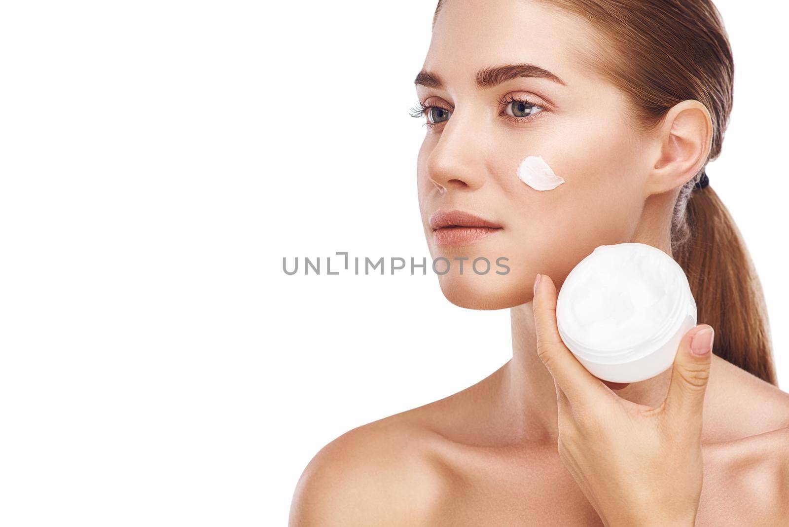 Beautiful womans right cheek with facecream close up studio photo on white background. Light hair, grey eyes