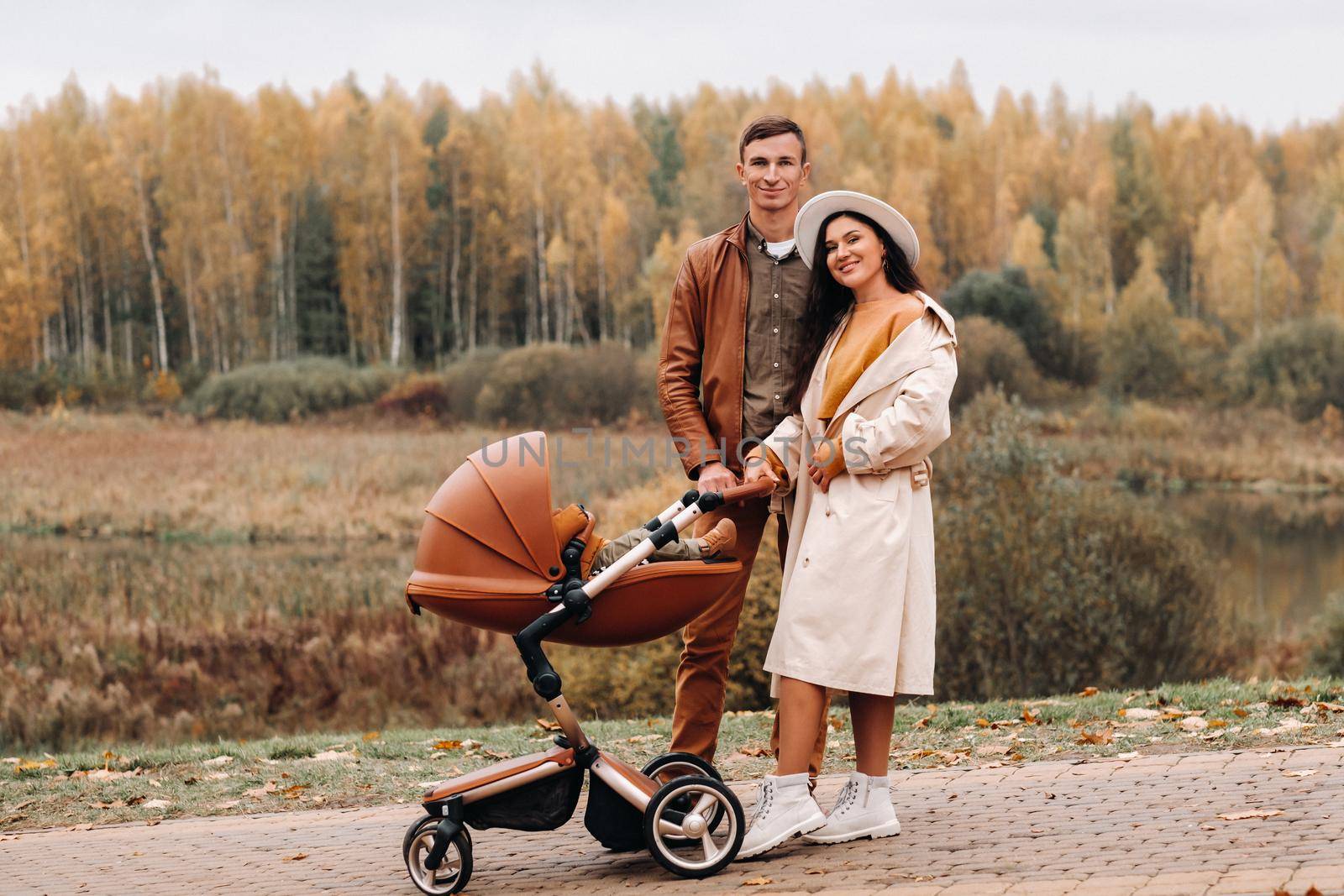 Father and mother on a walk with a stroller in the autumn Park. The family walks through the nature Park in the Golden autumn. by Lobachad