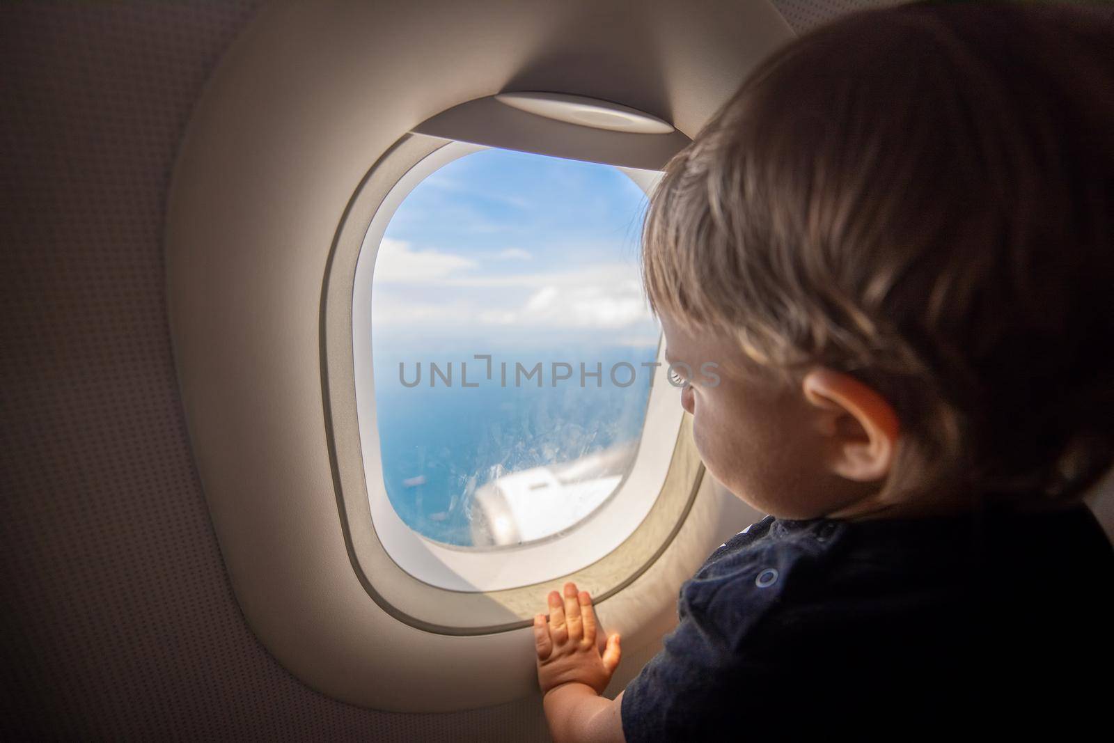 Toddler looks at the ground through the porthole of a flying plane. travel with children