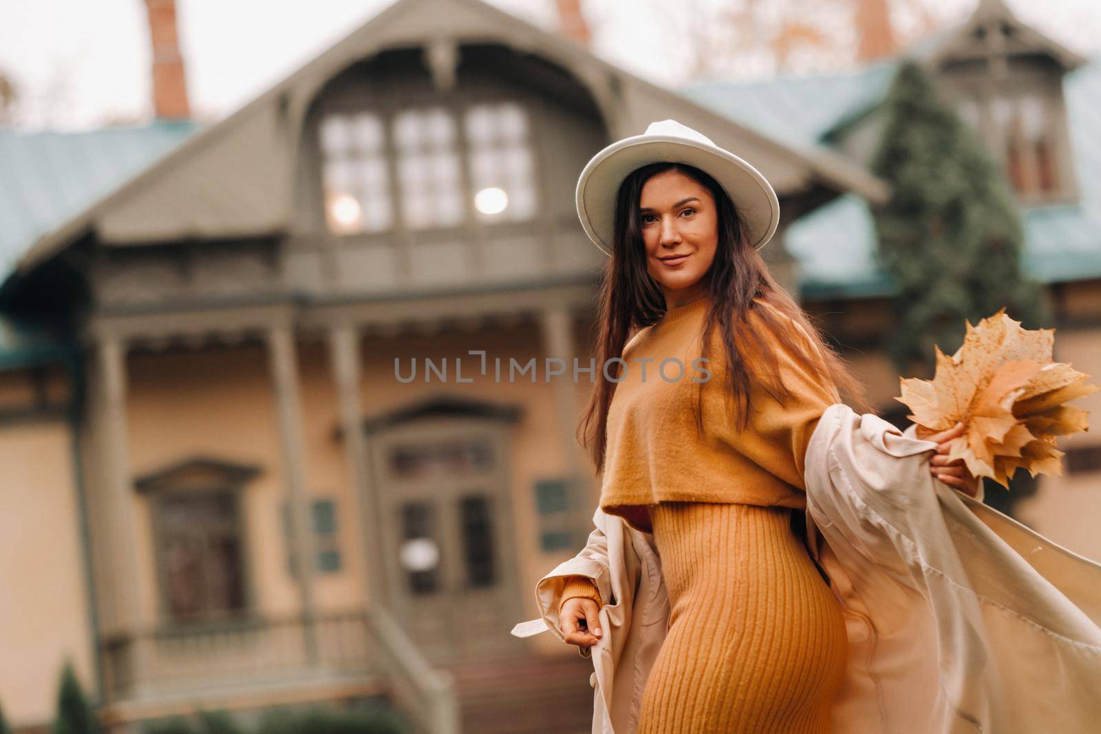 a girl in a white coat and hat smiles in an autumn Park.Portrait of a woman in Golden autumn. by Lobachad