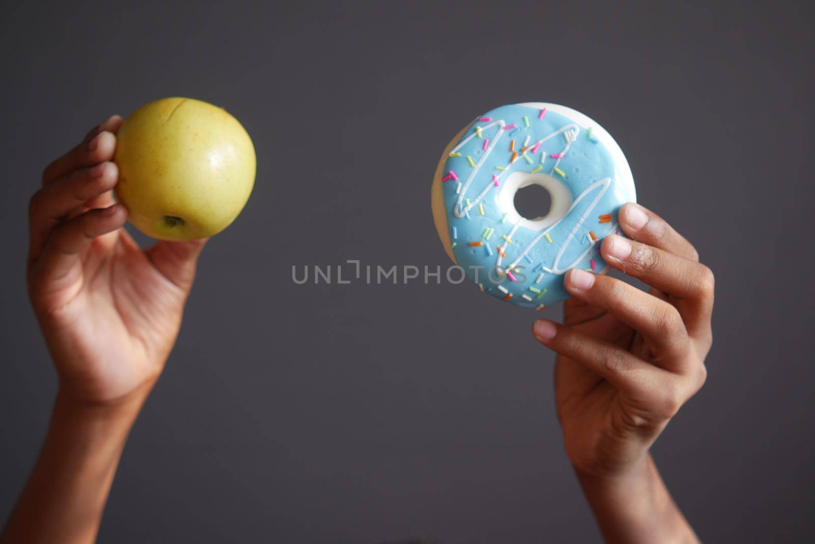 hand holding donuts and apple against gray background ,