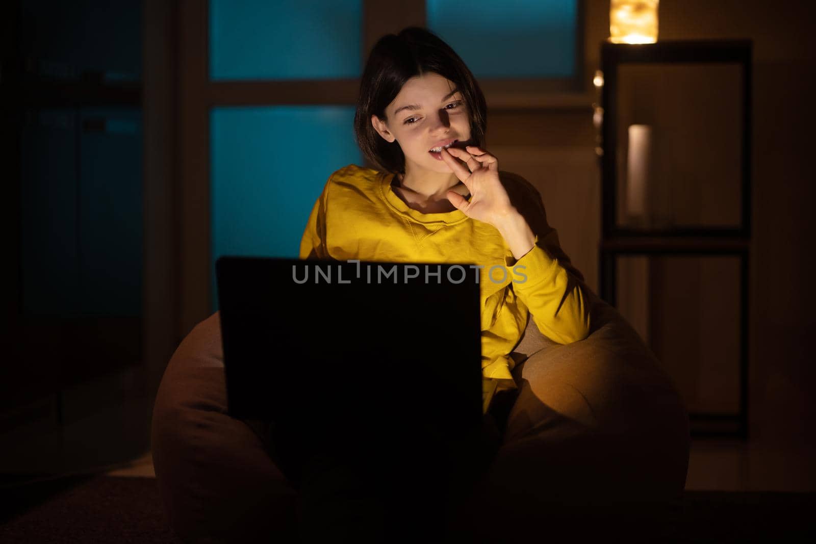 Portrait of beautiful caucasian girl uses laptop while sitting at home. In the evening creative woman works on a computer in her cozy living room.