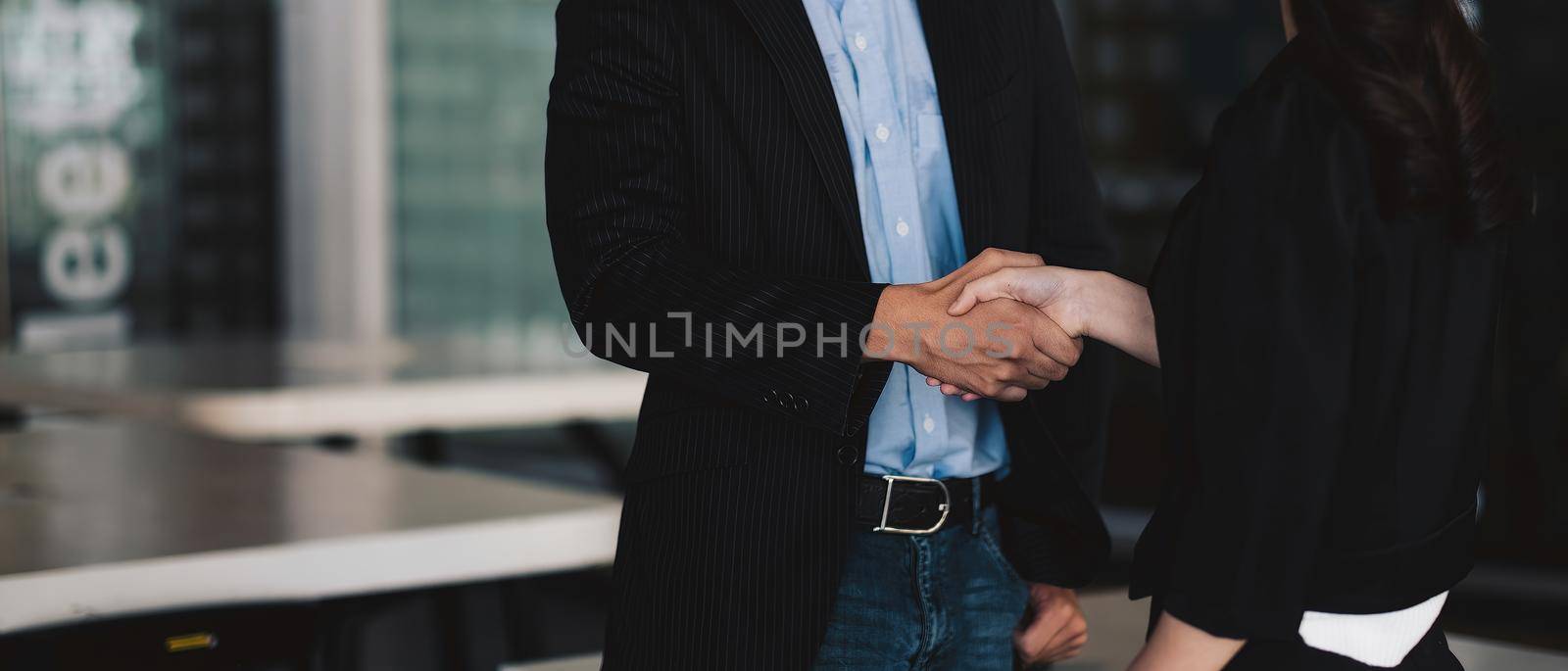 Happy positive business partners finishing meeting. Business man and woman standing in office, shaking hands, smiling, talking. Handshake concept.